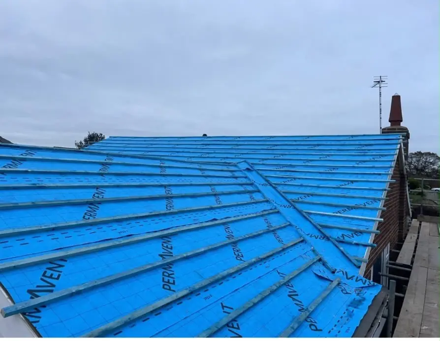 New blue breathable membrane laid over a hip roof, chimney at the far end