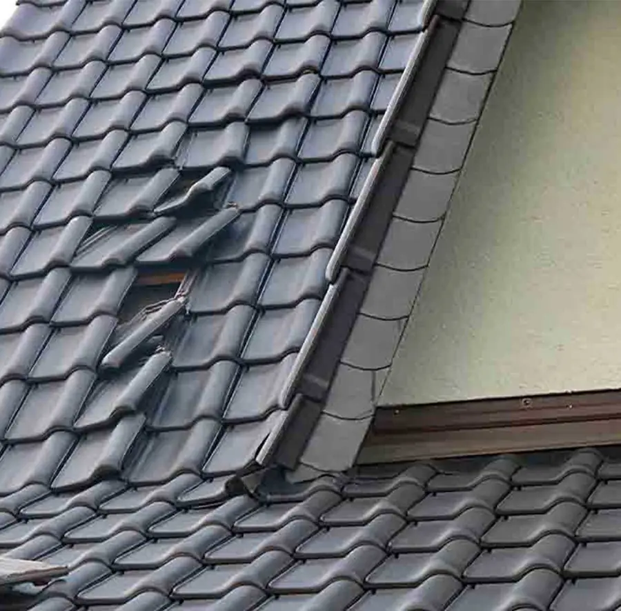 Lifted and broken tiles on a pitched roof beside lead flashing at a wall