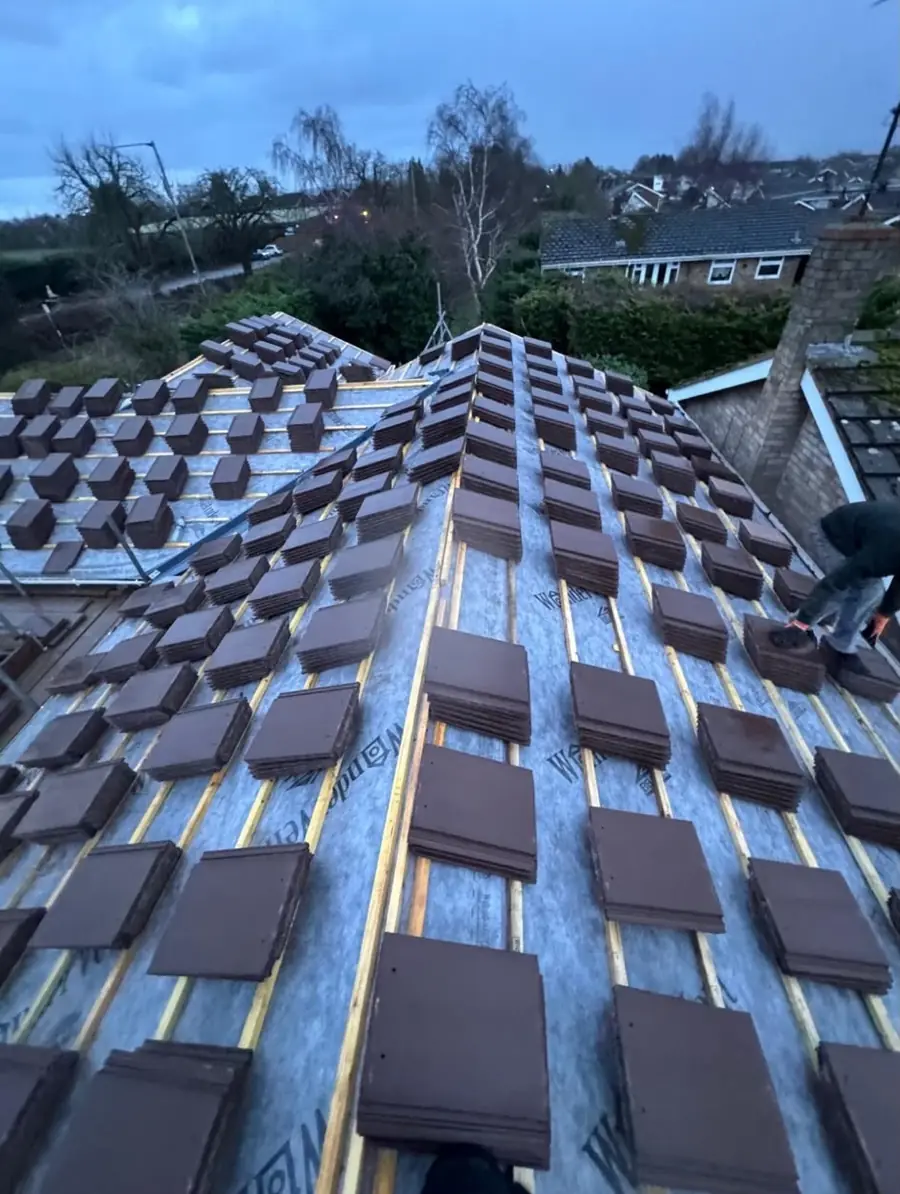 Brown tiles stacked over membrane and battens on a hip roof, ready to lay