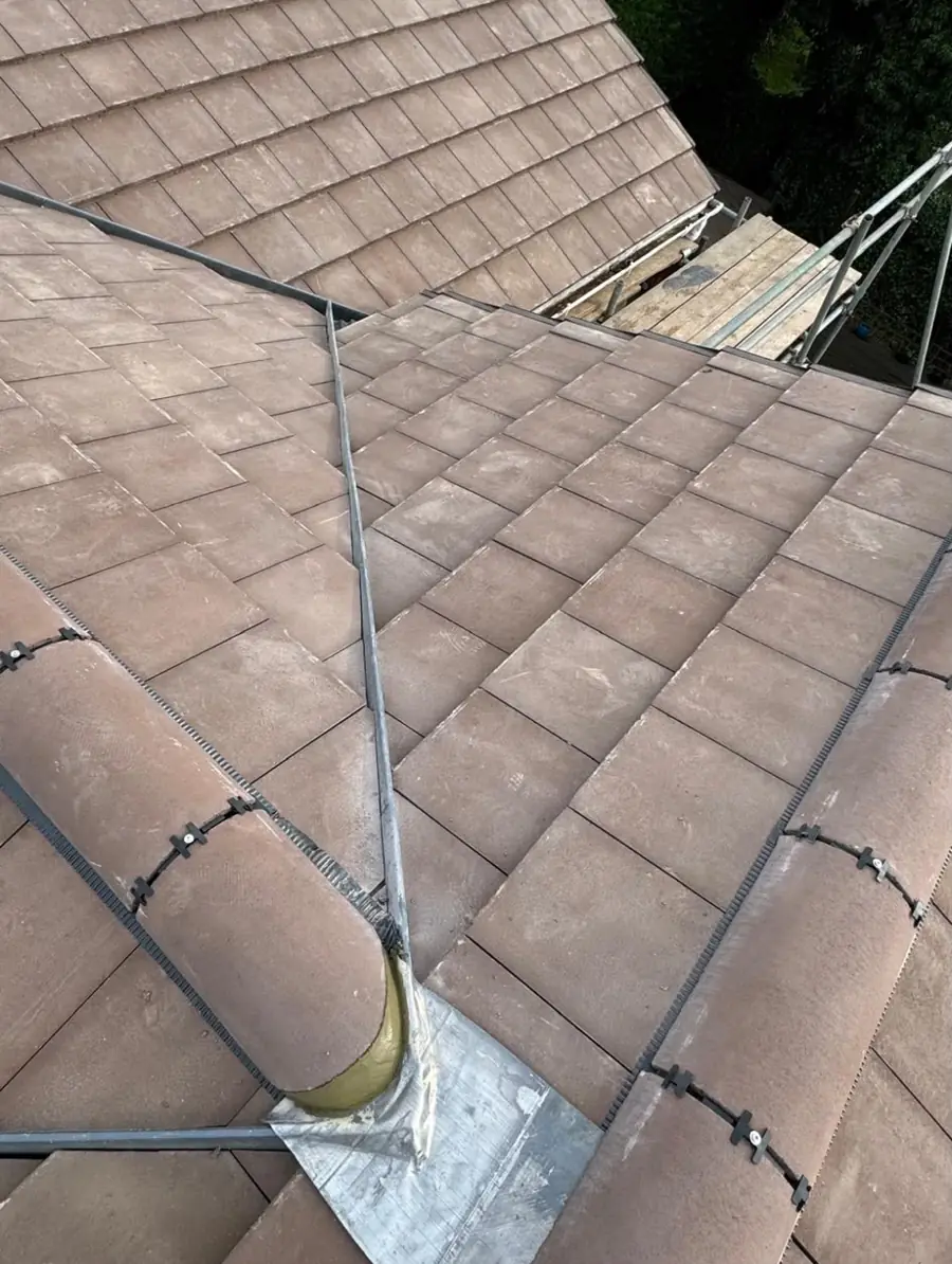 Close view of a brown tiled hip with the ridge tiles clipped down and a lead flashing at the base