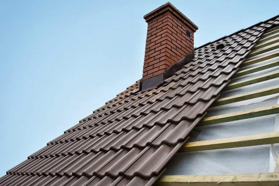 New brown tiles going on over membrane and battens beside a brick chimney