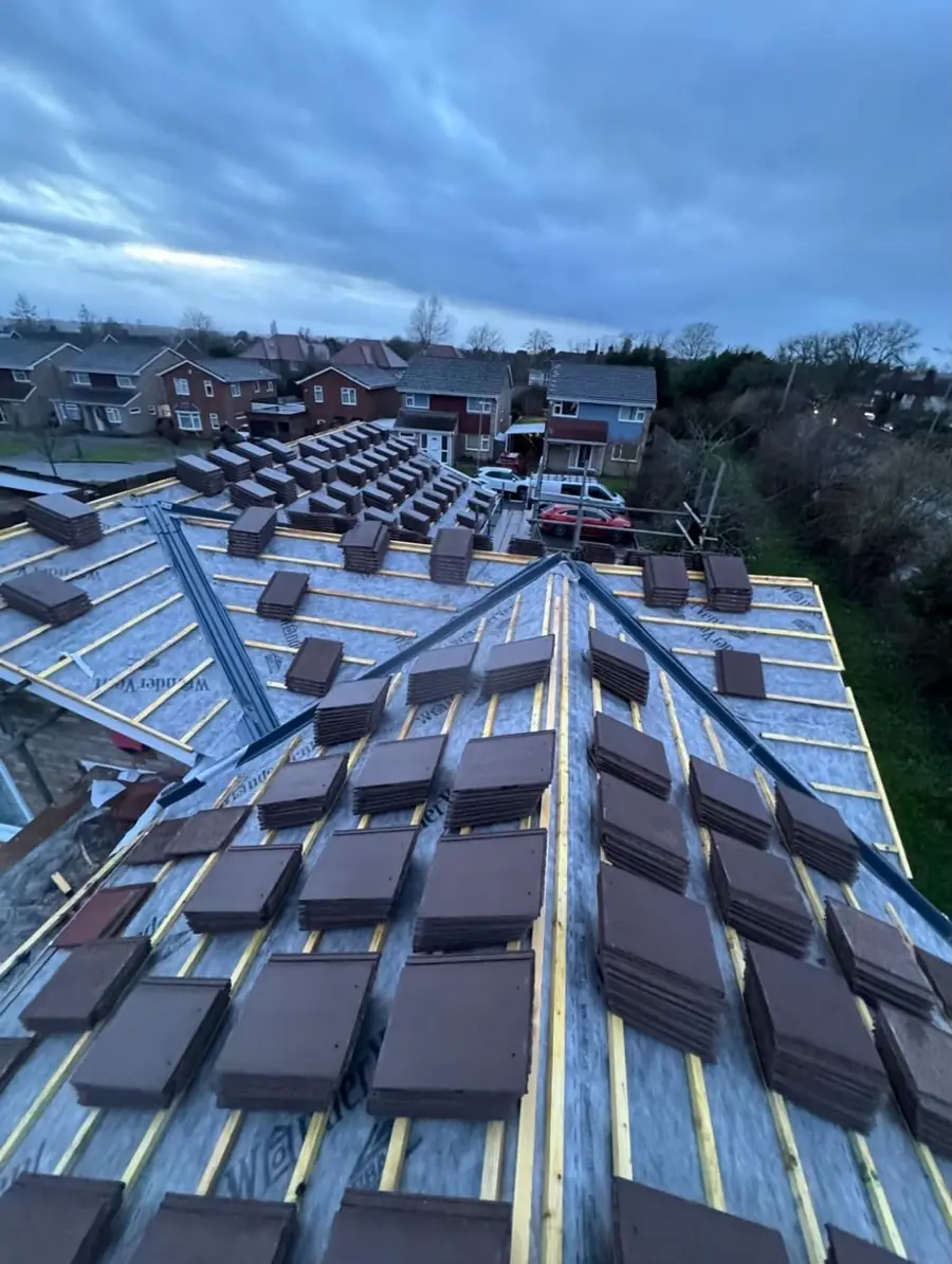 Bundles of brown tiles spread across the battens ready to be laid, houses behind