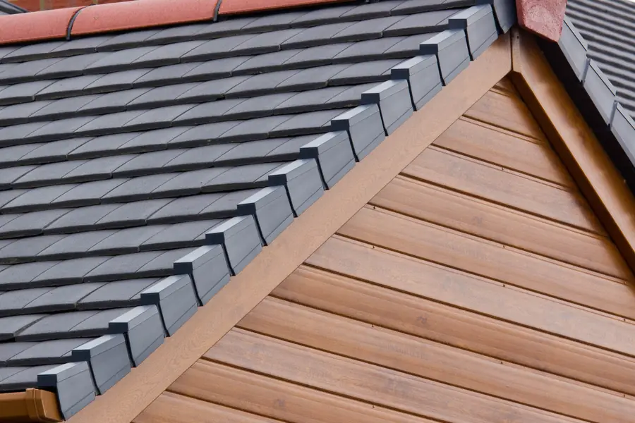 Dark tiled roof with a red ridge and neat verge above a timber-effect gable