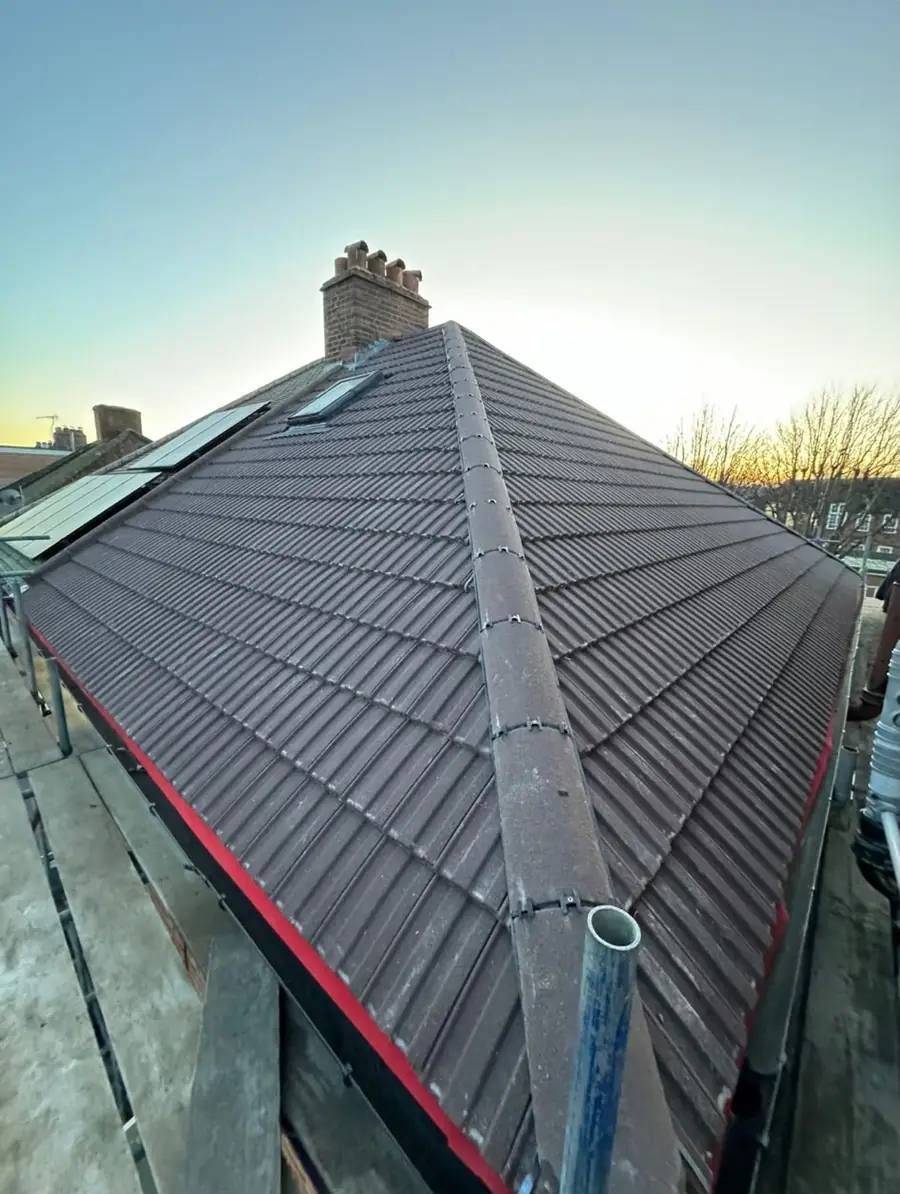 Dark tiled hip roof with a ridge, roof windows and a chimney stack in low evening light