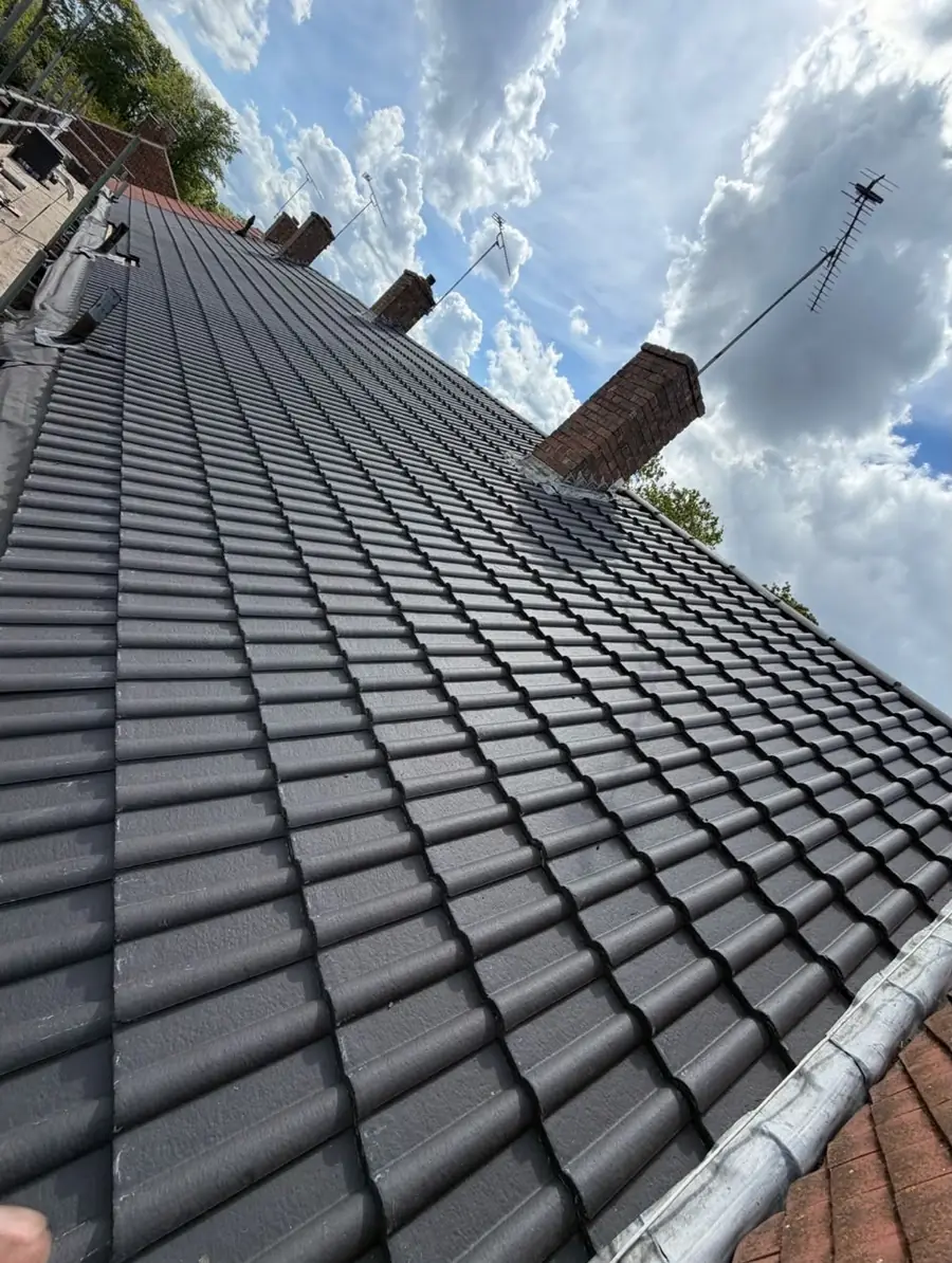 Rows of dark tiles running up to a brick chimney under a blue and cloudy sky