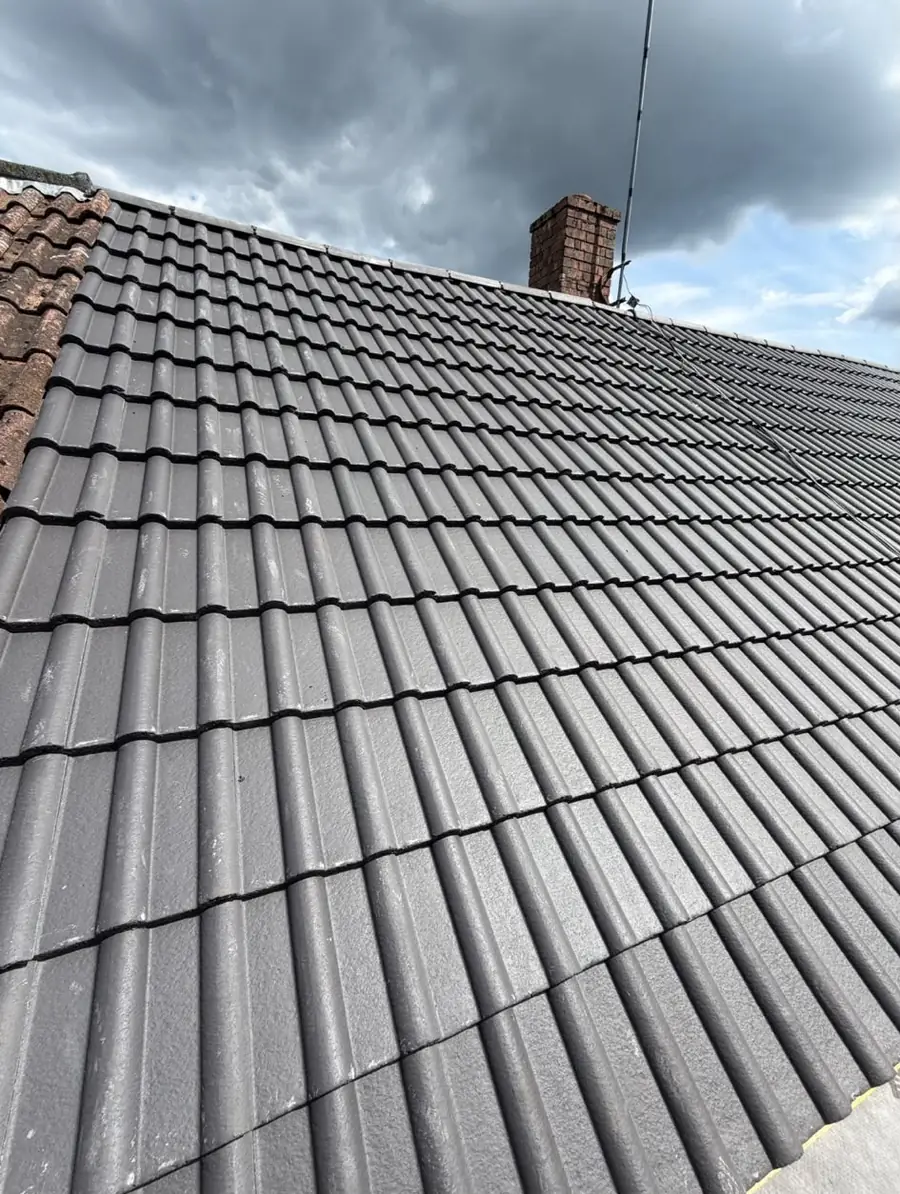 Grey tiled roof with a brick chimney and aerial under a cloudy sky