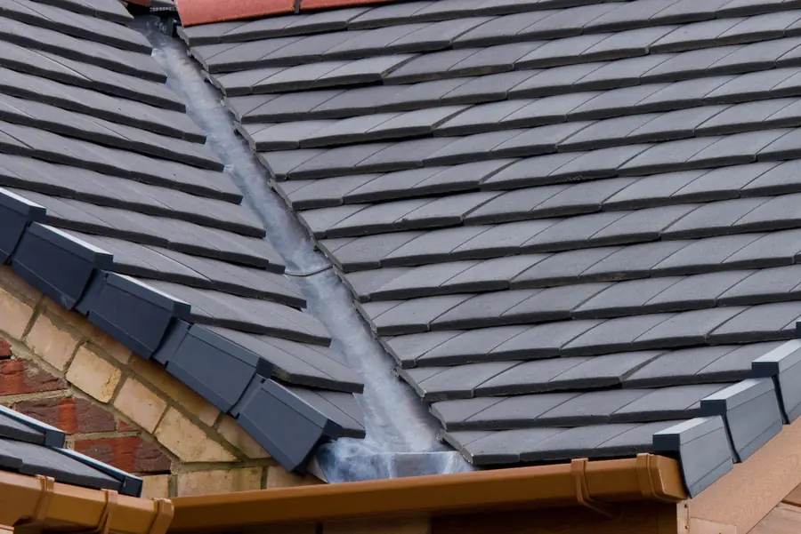 Lead valley running down a dark tiled roof into a brown gutter