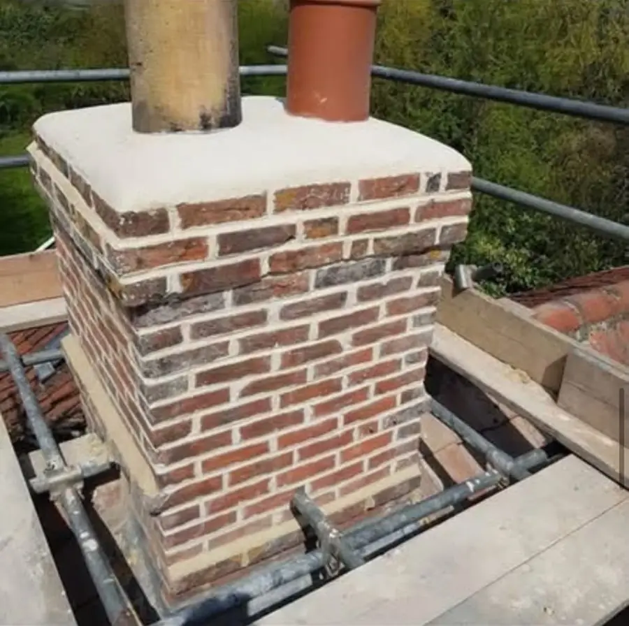 Rebuilt brick chimney stack with clean pointing and a new mortar cap, scaffold round it