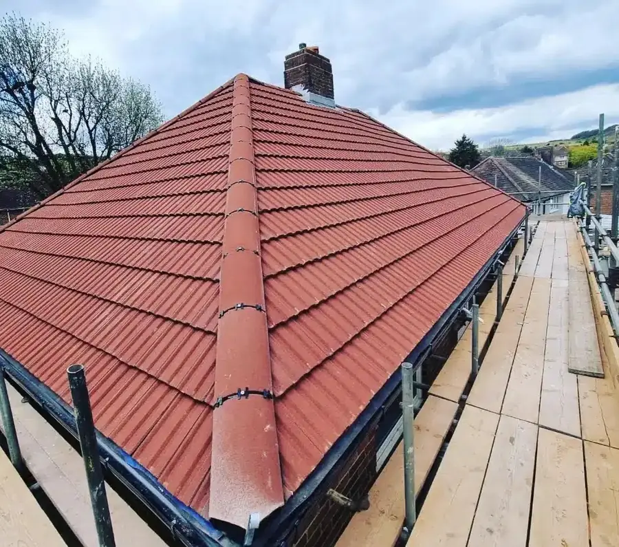 New red tiled hip roof with a finished ridge and a scaffold walkway along the eaves