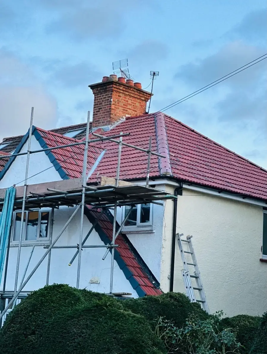 Red tiled roof and brick chimney above a white rendered house with scaffold up