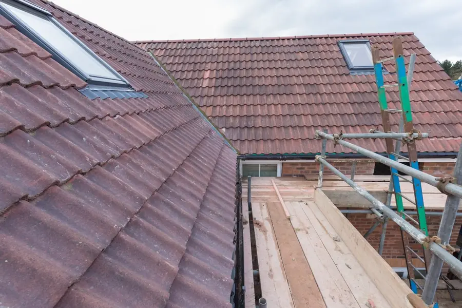 Red-brown tiled roof with roof windows and scaffold boards beside a dormer