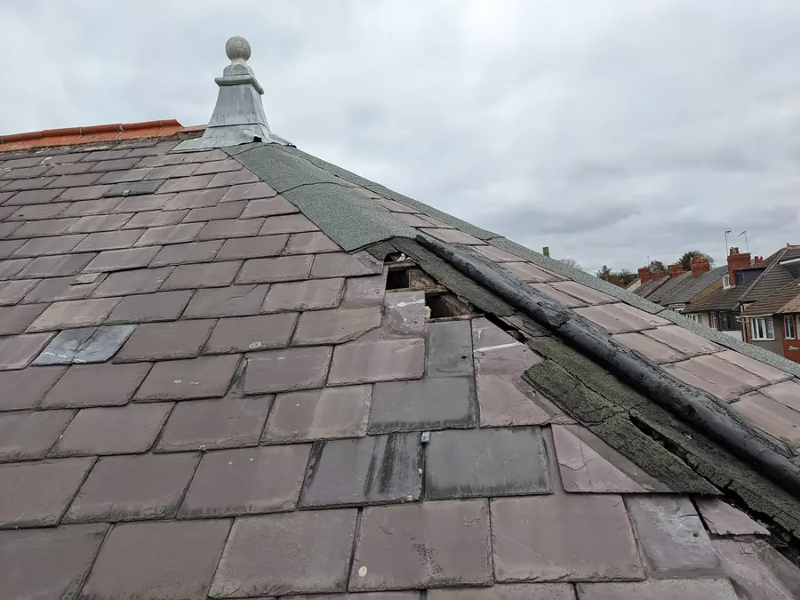 Weathered slate hip roof with missing slates and a split hip covering