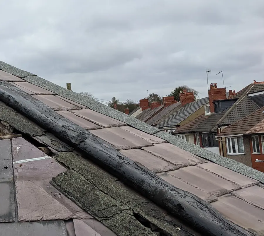 Failing hip covering and slipped slates on an old slate roof, houses beyond
