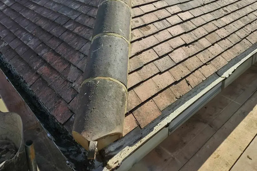 End of an old ridge tile above a stained gutter, scaffold boards below