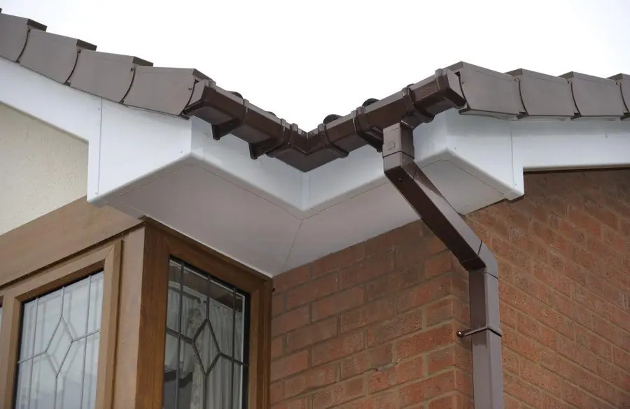 White soffit and fascia with a brown gutter and downpipe beside a bay window
