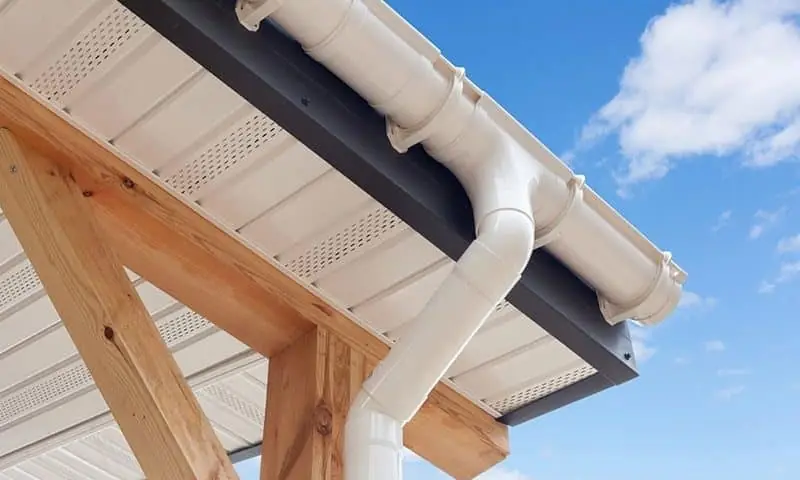 White vented soffit, fascia and gutter with a downpipe, seen from below against blue sky