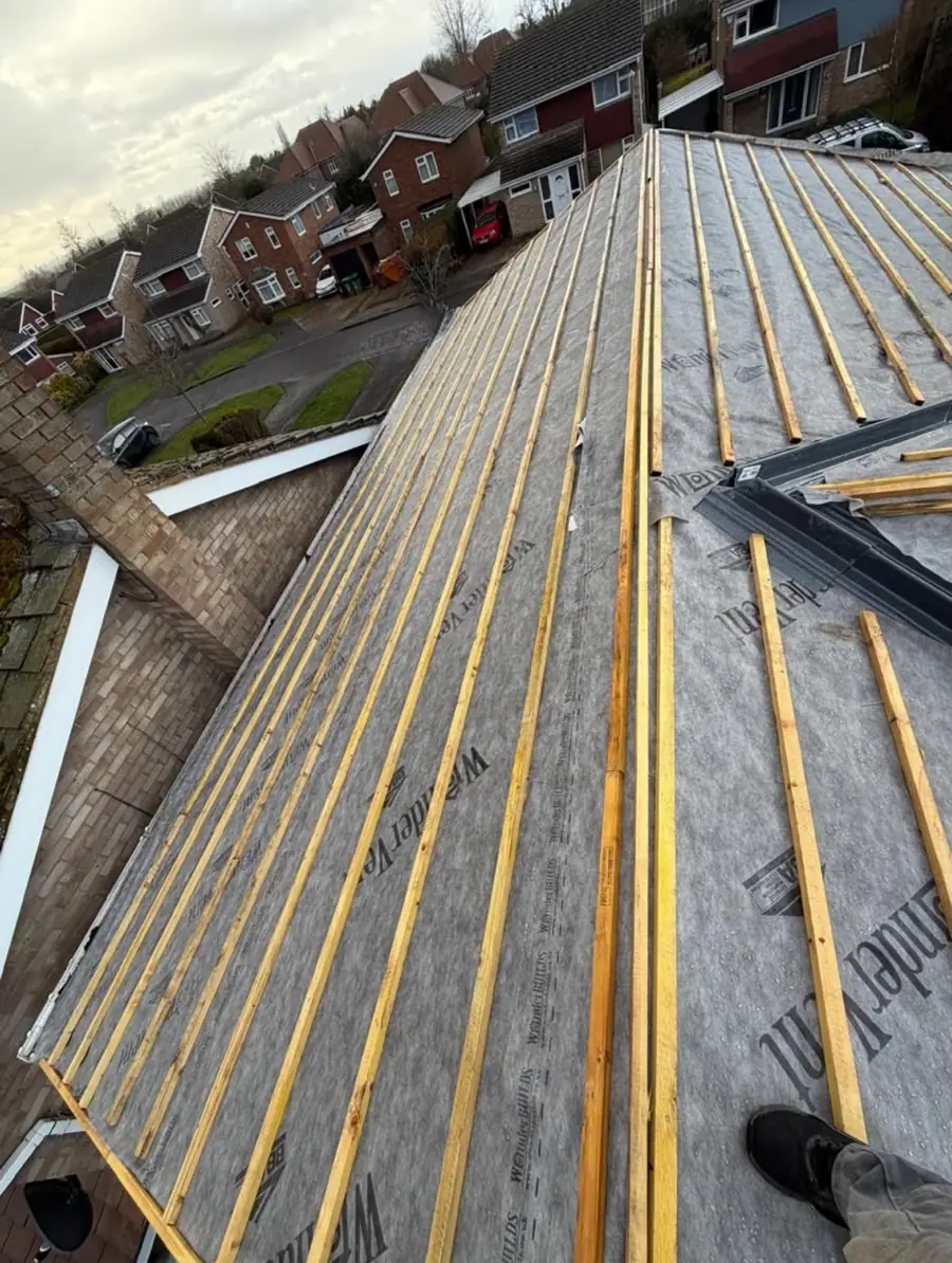 Roof slope stripped to breathable membrane and yellow battens, houses below
